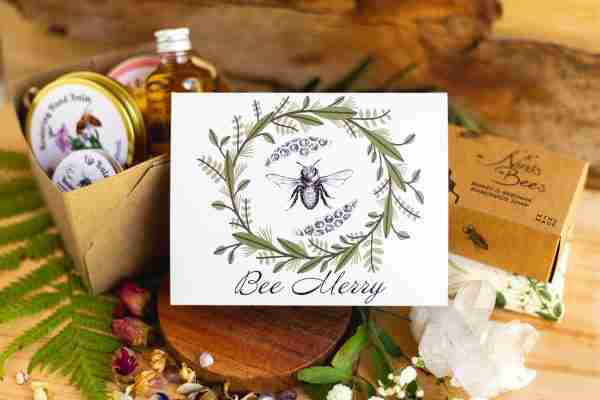 Bee Merry" eco-friendly greeting card by Nina's Bees, printed on recycled matte paper with a bee and greenery design.