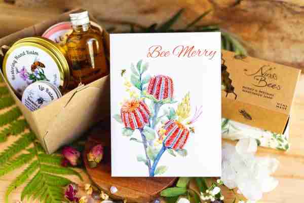 Bee Merry" eco-friendly floral greeting card by Nina's Bees, featuring vibrant Australian native Banksia flowers and a honey bee design, printed on recycled matte paper.