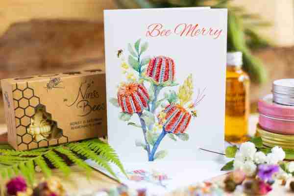 Bee Merry" eco-friendly floral greeting card by Nina's Bees, featuring vibrant flowers and a bee design, printed on recycled matte paper.