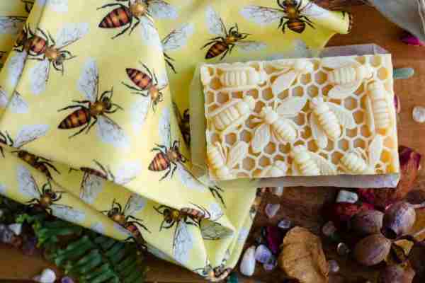 Handcrafted honey and beeswax soap with a raised honeycomb and bee design, placed on a yellow bee-print cloth surrounded by natural botanicals.